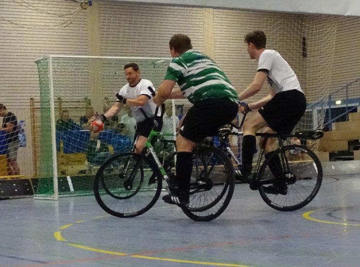 Martin Egarter und Thomas Kieferle während eines Radballspiels,
			  wobei Martin Egarter einen vom Gegenspieler auf das Tor geschossenen Ball mit der Hand abwehrt.