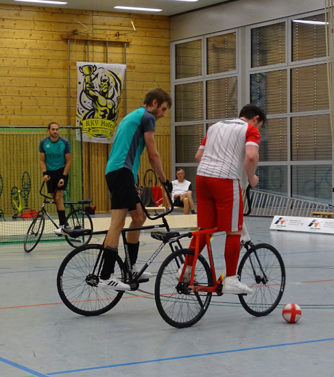 Foto eines Radballspiels, bei dem ein Torwart und dessen Feldspieler in der Verteidigung eines Angriffs zu sehen sind..